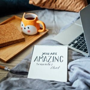 Positive daily affirmations for self love. Words You Are Amazing in notebook near laptop and tea